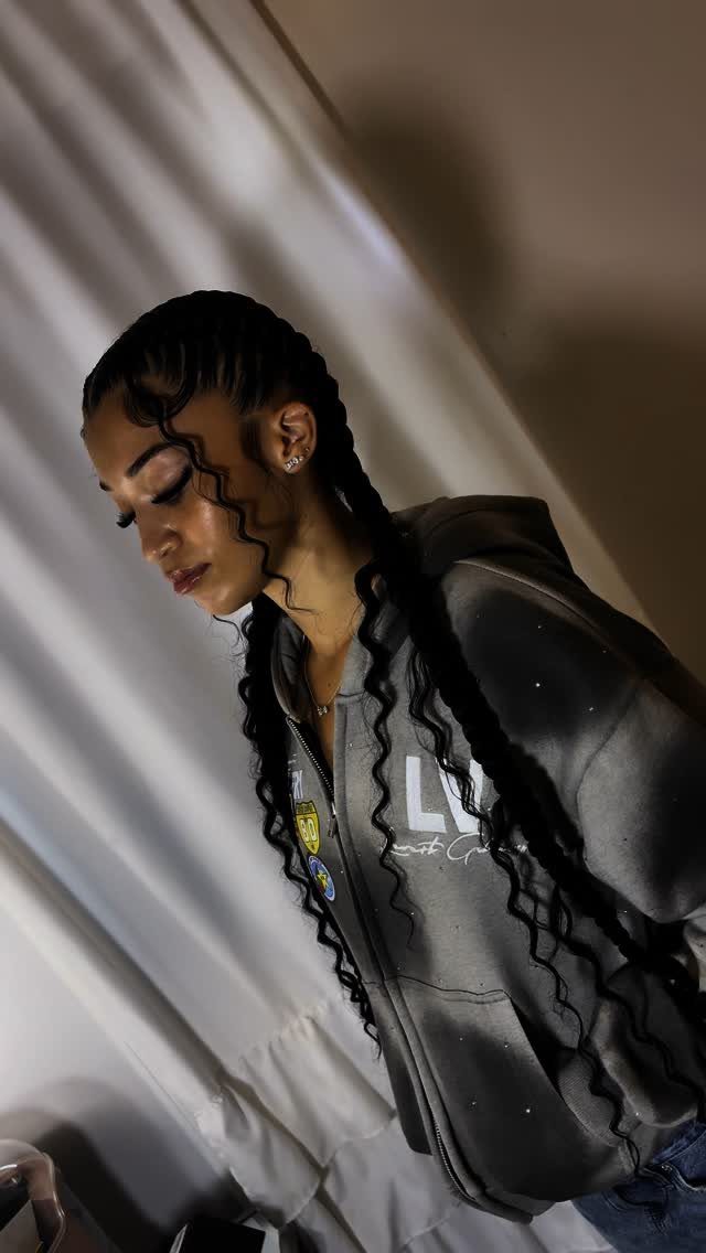 Woman with two long boho braids featuring curly strands wearing a grey hoodie.