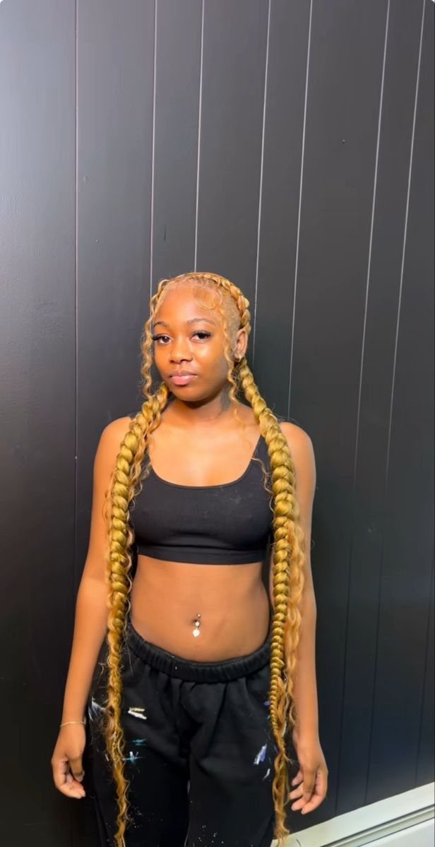 Woman with long honey-blonde braided pigtails and curly ends wearing black athletic wear.