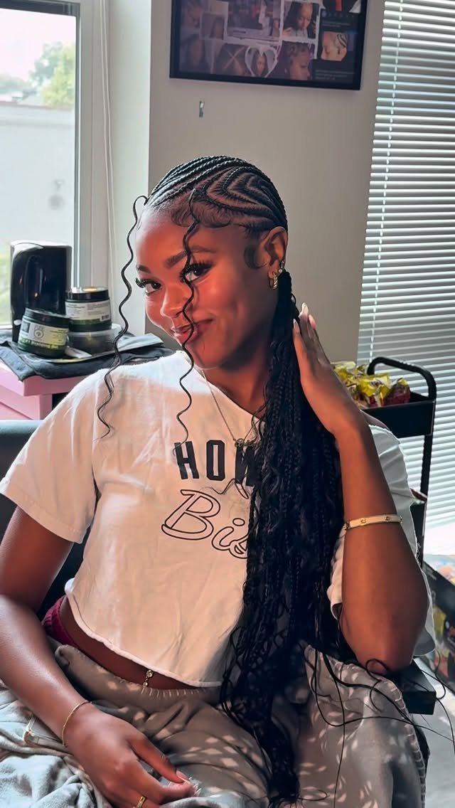 16 Big Cornrow Hairstyles for Bold, Standout Looks 12 Woman with cornrow braids and long curly extensions wearing a white t-shirt.