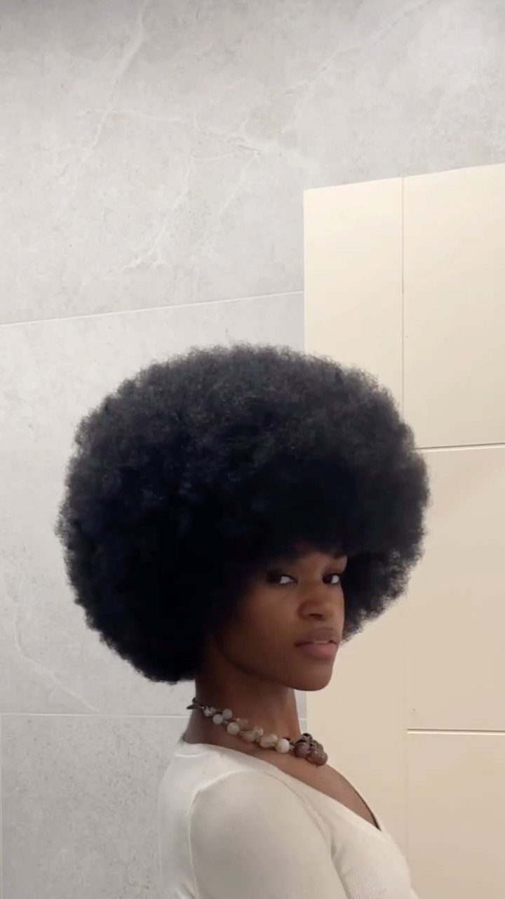 31 Black Hair Natural Hairstyles for Every Length 2 Woman with a large, voluminous black afro hairstyle wearing a white top.