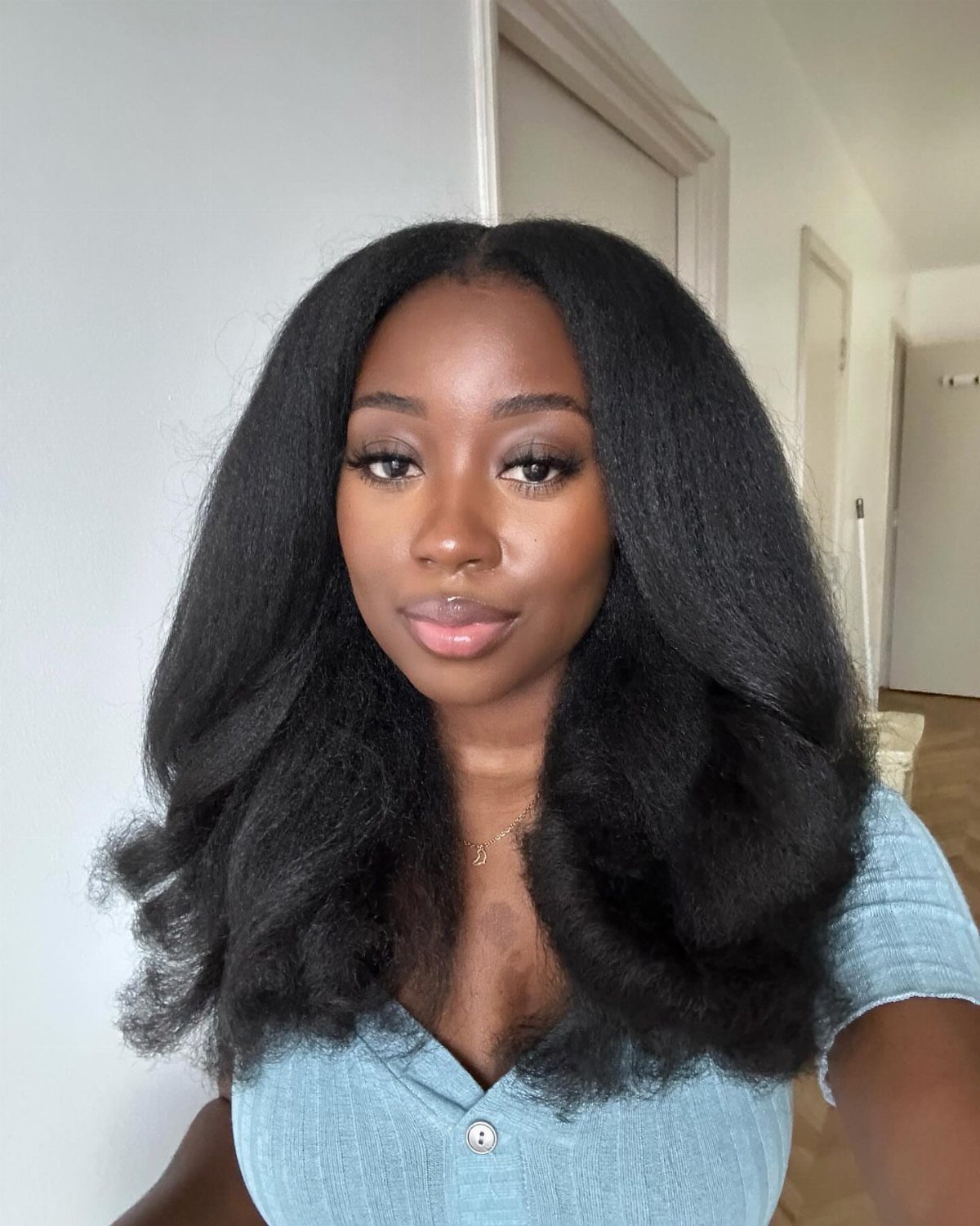31 Black Hair Natural Hairstyles for Every Length 16 Woman with voluminous black blowout hair wearing a light blue button-up shirt.
