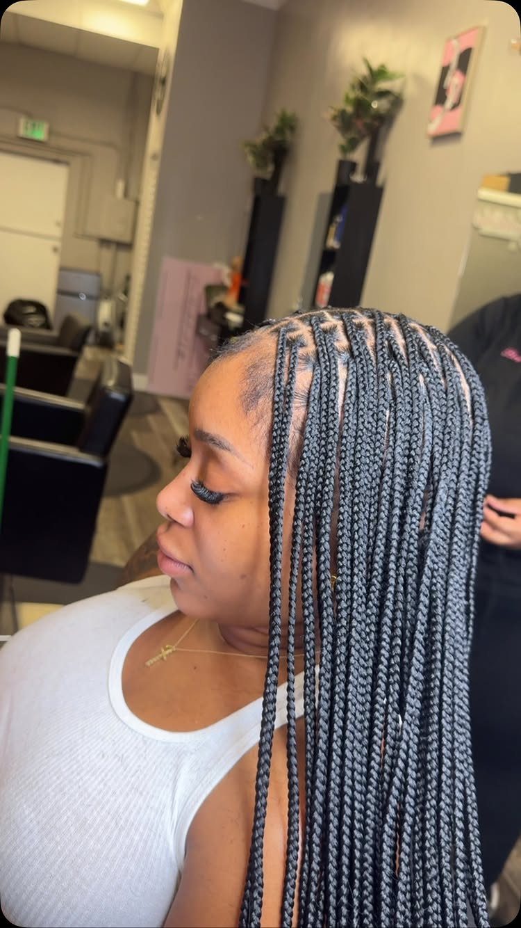 31 Black Hair Natural Hairstyles for Every Length 1 Woman with long black box braids wearing a white tank top in a salon