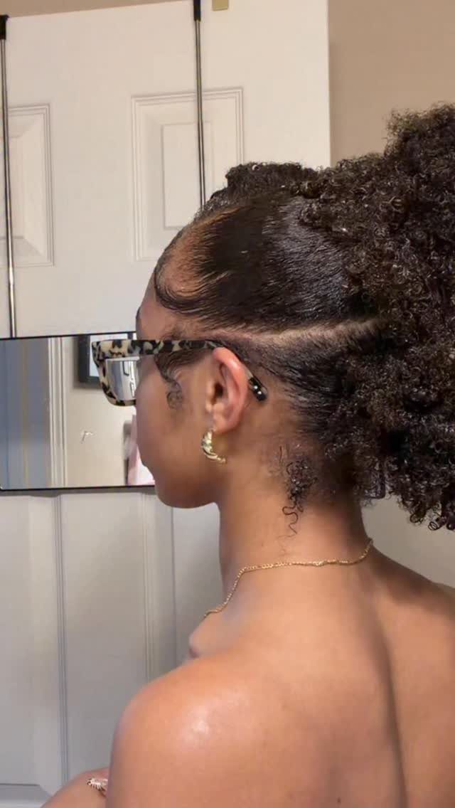 31 Black Hair Natural Hairstyles for Every Length 10 Woman with slicked-back sides and a high curly puff hairstyle wearing glasses.