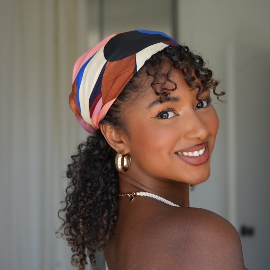 31 Black Hair Natural Hairstyles for Every Length 19 Woman with curly black hair wearing a colorful patterned head wrap and gold earrings.