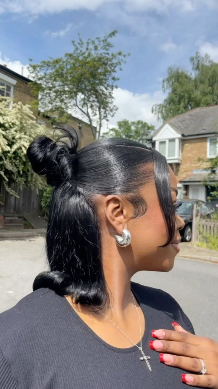 31 Black Hair Natural Hairstyles for Every Length 26 Woman with sleek black hair in a half-up bun posing outdoors.