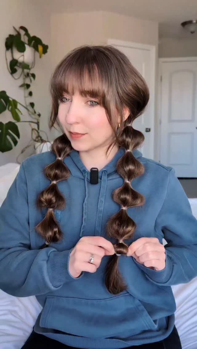 15 Braid Hairstyles for Thick Hair, From Bubble to Boho 3 Woman with brown hair creating two bubble braids while wearing a blue hoodie.