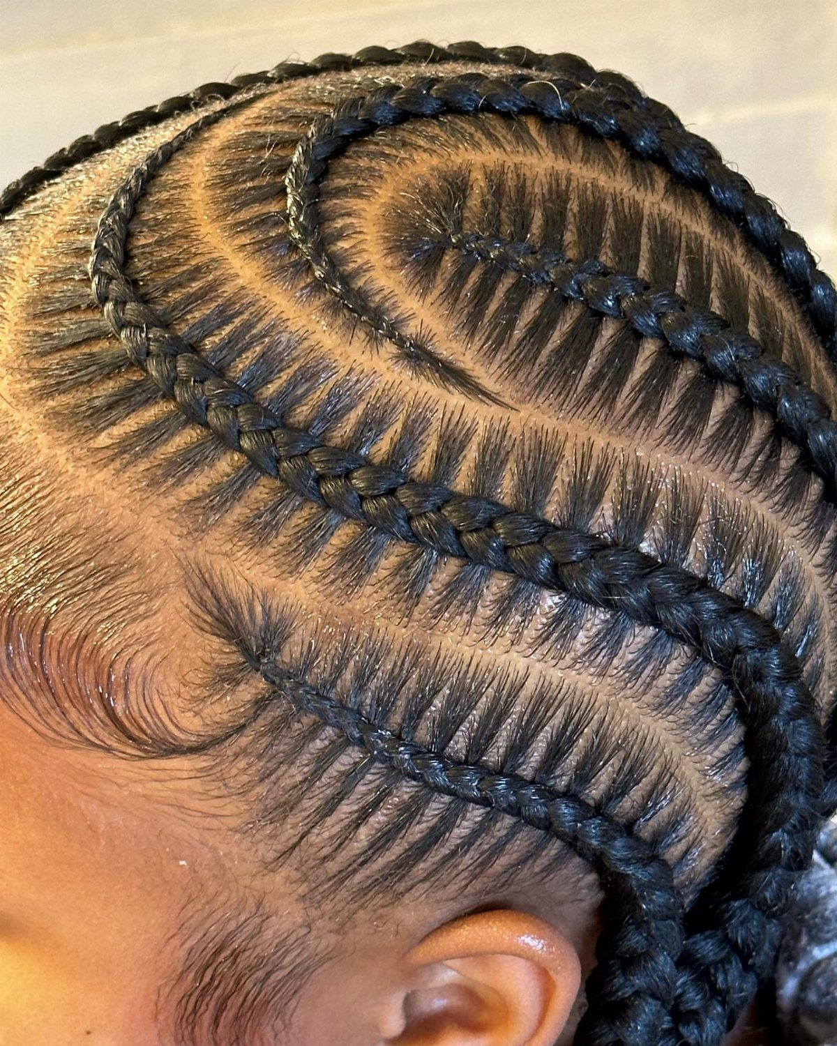 15 Braid Hairstyles for Thick Hair, From Bubble to Boho 9 Curved black stitch braids with precise parting and styled edges on a person.