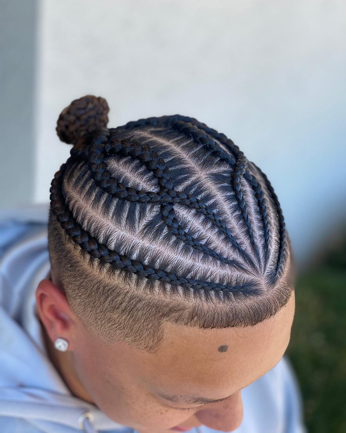 11 Braided Mens Hairstyles: Cornrows, Box Braids and More 3 Man with intricate cornrow braids styled into a small bun and side fade.