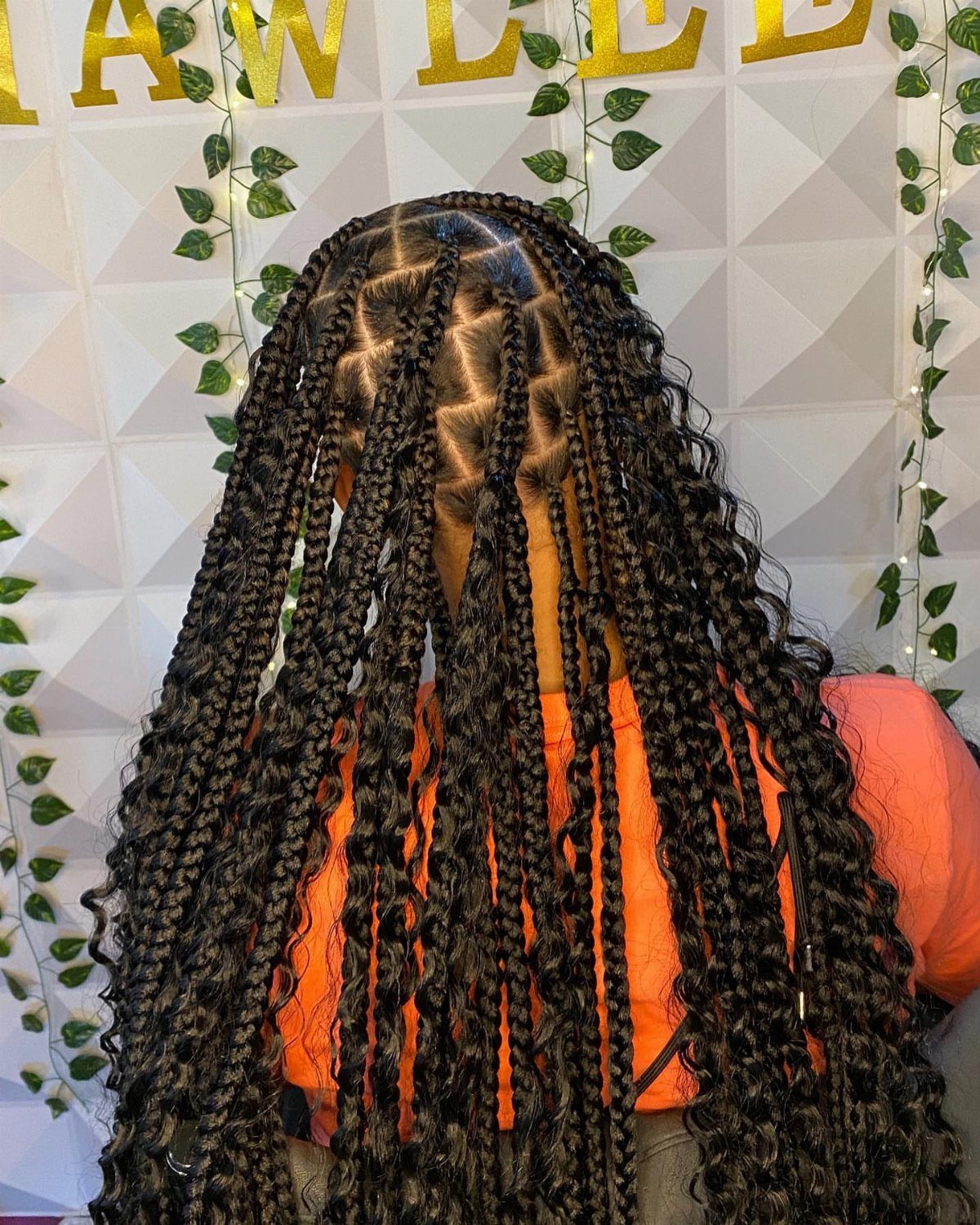 16 Braids Going Back with Curls: Styles to Try 5 Long black box braids with voluminous curls on a person wearing orange.