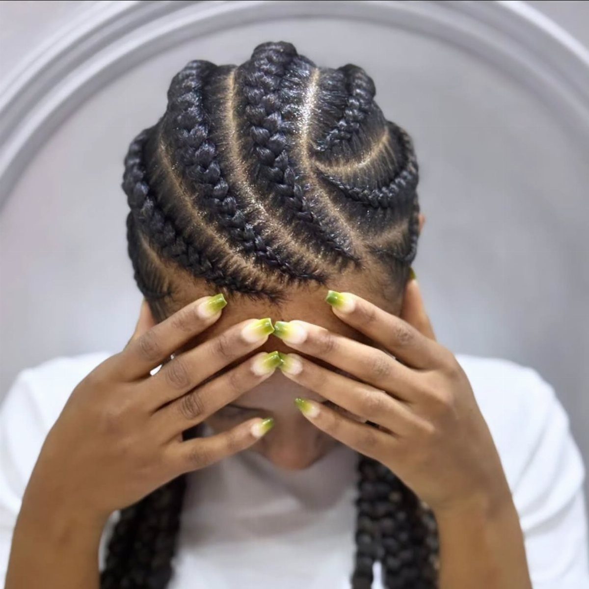 9 Braids with Natural Hair Only: Styles Without Extensions 1 Person with curved cornrows hairstyle covering their face with manicured hands.