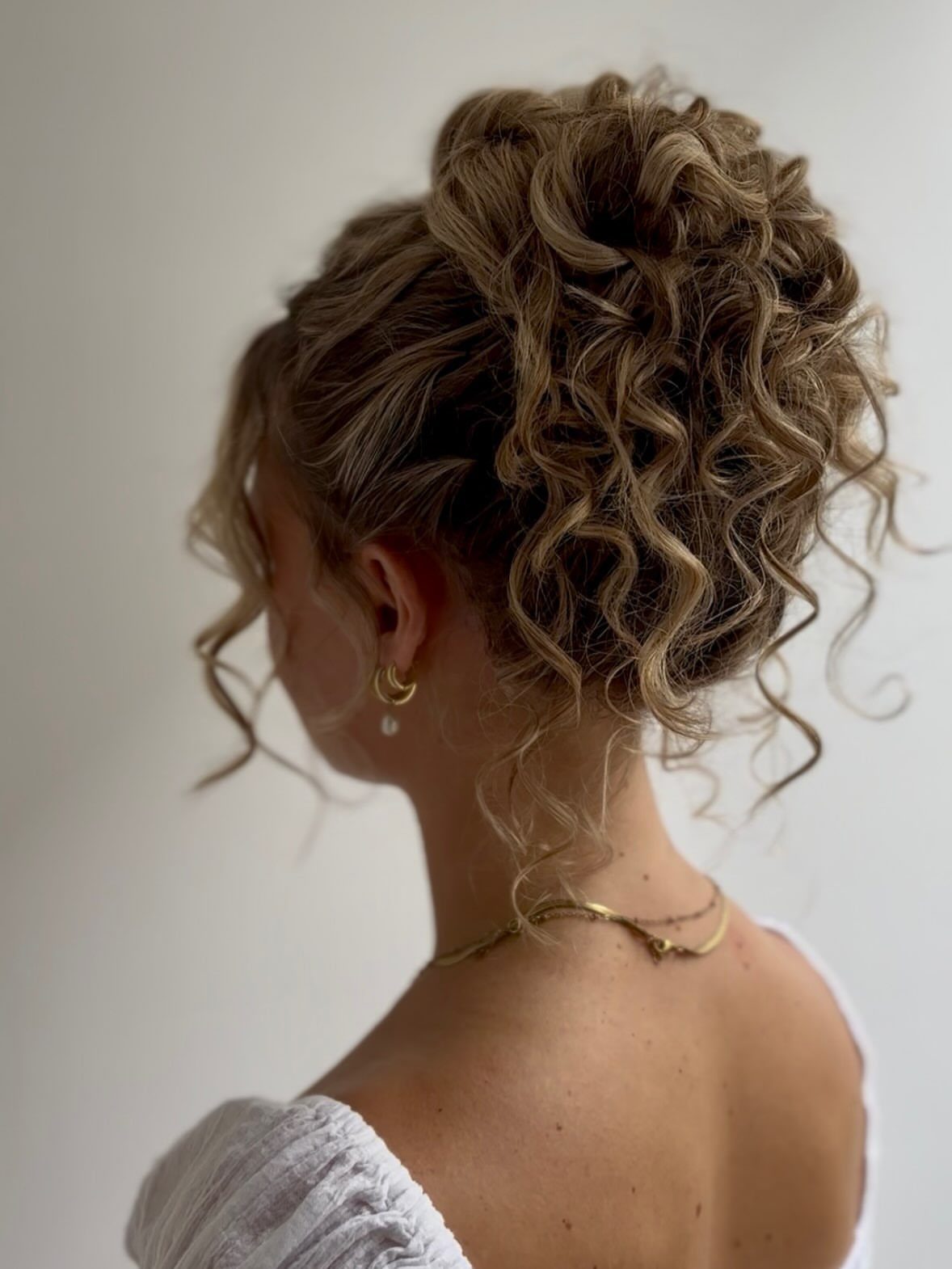 8 Ideas for a Bun with Curls, From High to Low 1 Blonde hair styled in a high bun with tight, defined curls and loose tendrils.