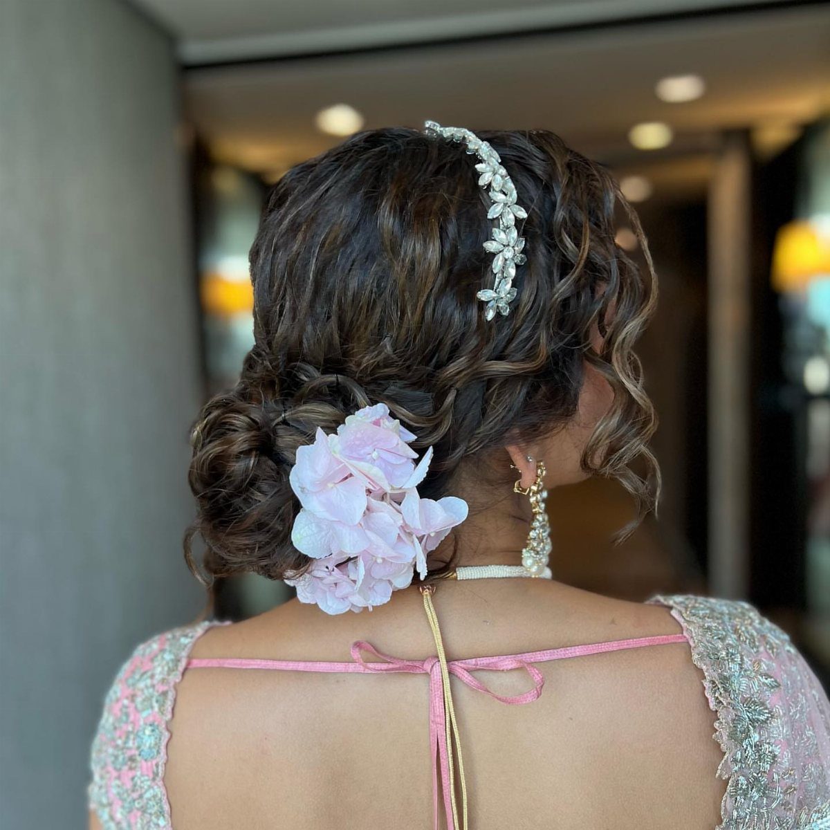 Buns for Curly Hair: 7 Ideas, From Messy to Floral 7 Low curly hair bun decorated with a pink flower and silver headband.