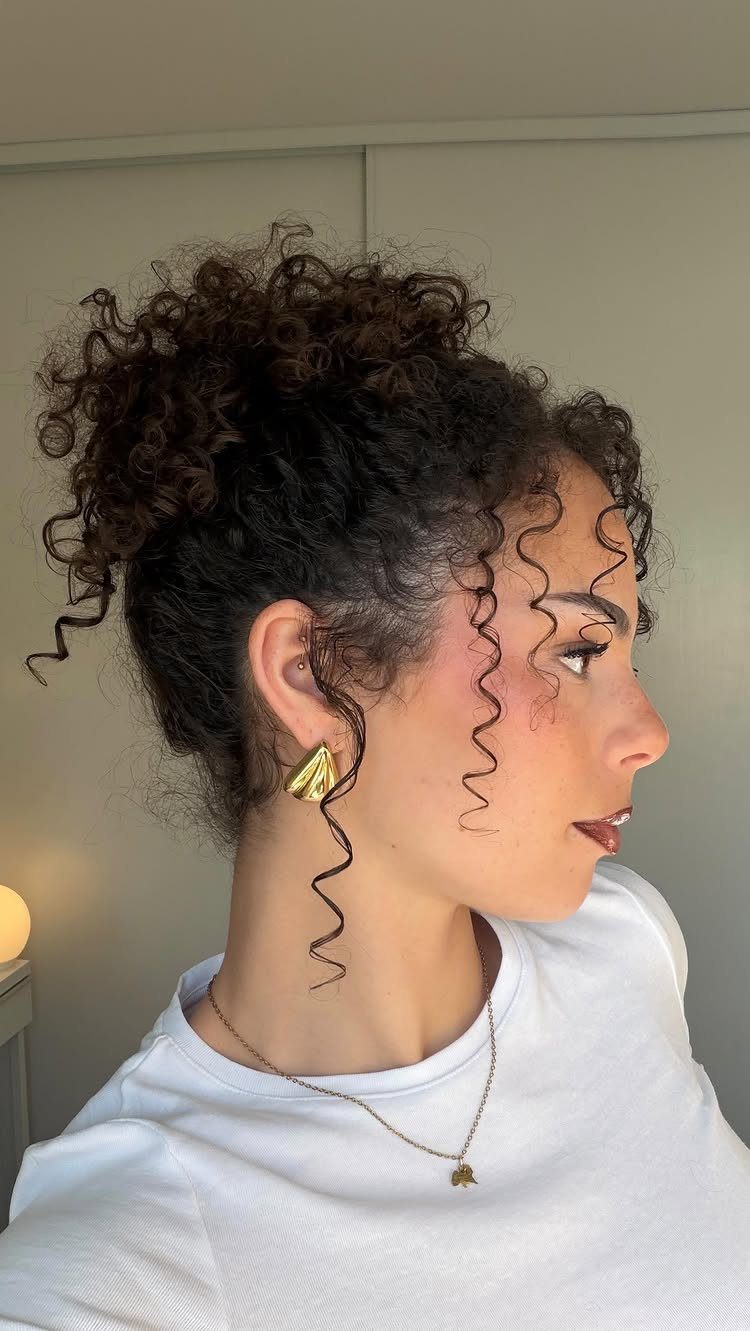 Buns for Curly Hair: 7 Ideas, From Messy to Floral 1 Woman with curly hair styled in a high messy bun and face-framing curls.