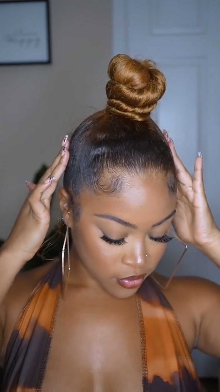 Buns for Curly Hair: 7 Ideas, From Messy to Floral 4 Woman with a golden-brown top knot bun and patterned orange dress posing indoors.