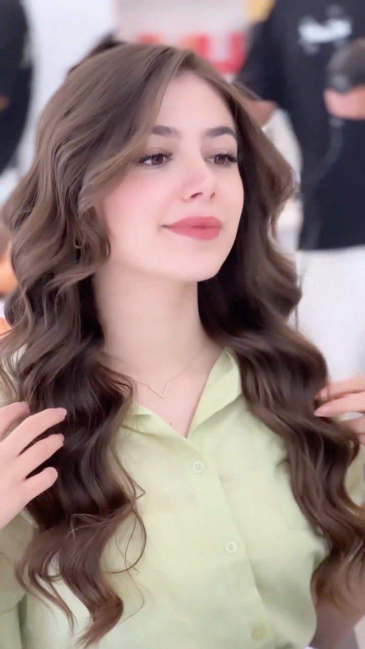 9 Business Casual Hairstyles for Women at the Office 5 Woman with long brown hair styled in soft waves wearing a green shirt.
