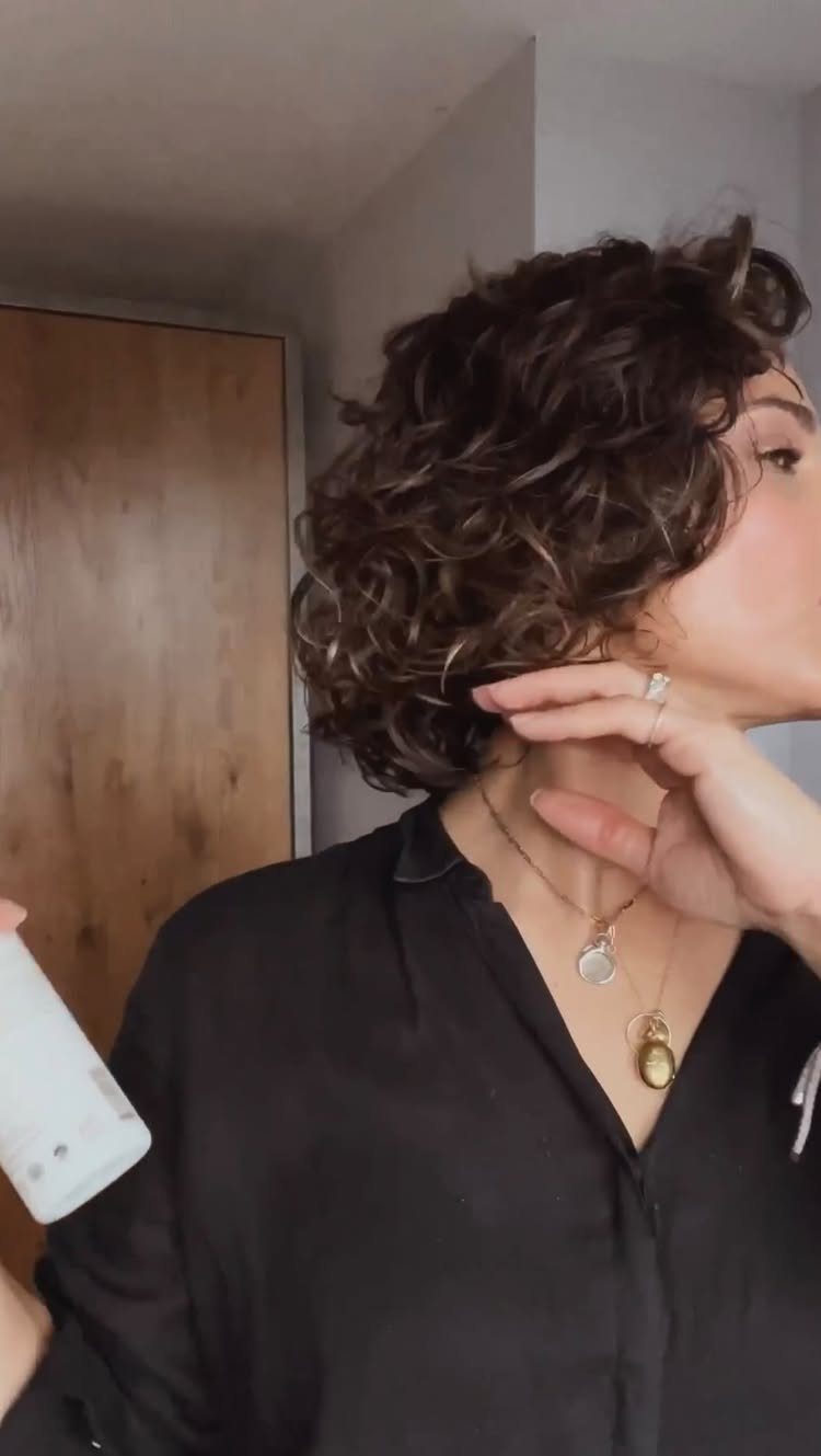 9 Business Casual Hairstyles for Women at the Office 7 Woman with a curly brown bob hairstyle wearing a black shirt and gold necklaces.
