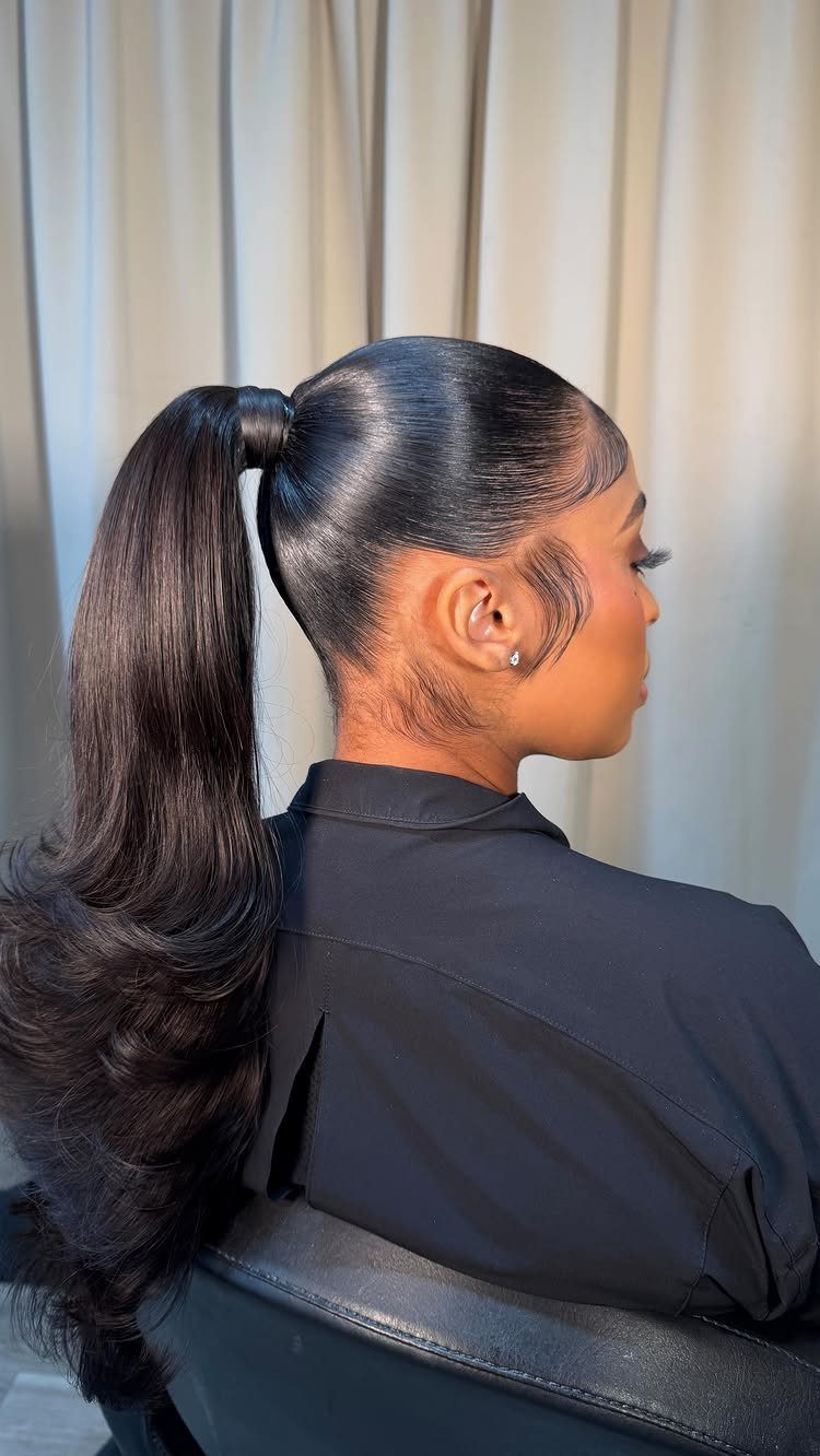7 Clean Look Hair Ideas for Sleek Buns and Ponytails 1 Woman with a sleek high ponytail and smooth edges against a beige curtain.
