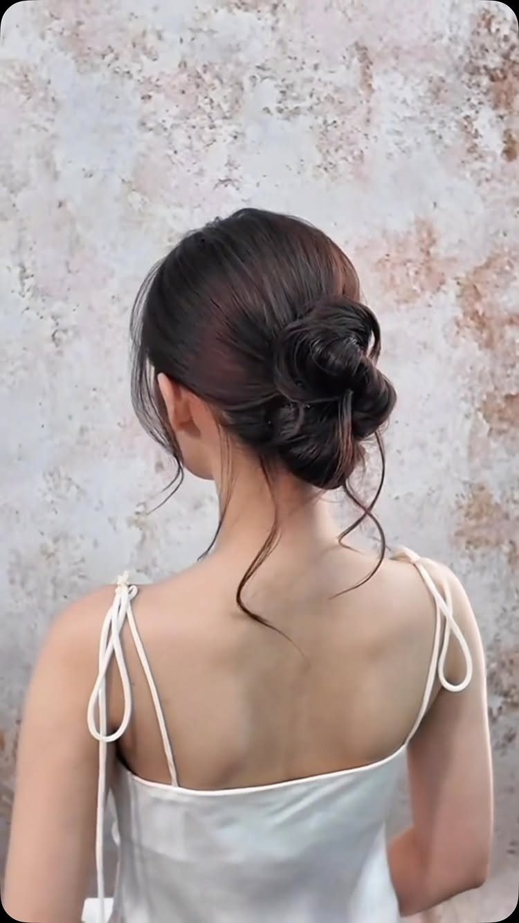 7 Clean Look Hair Ideas for Sleek Buns and Ponytails 4 Low twisted bun hairstyle on dark brown hair with loose face-framing strands.