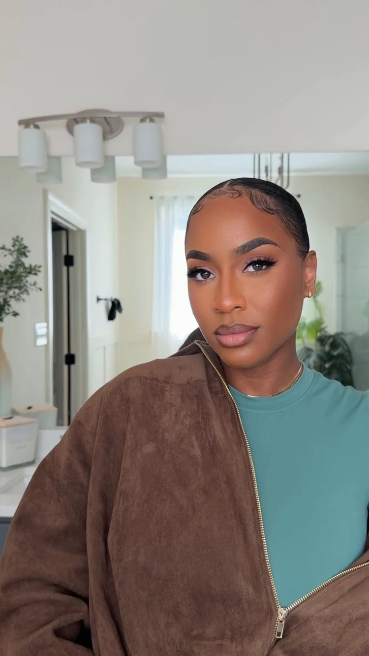 7 Clean Look Hair Ideas for Sleek Buns and Ponytails 7 Woman with slicked-back hair and styled baby hairs wearing a brown suede jacket.