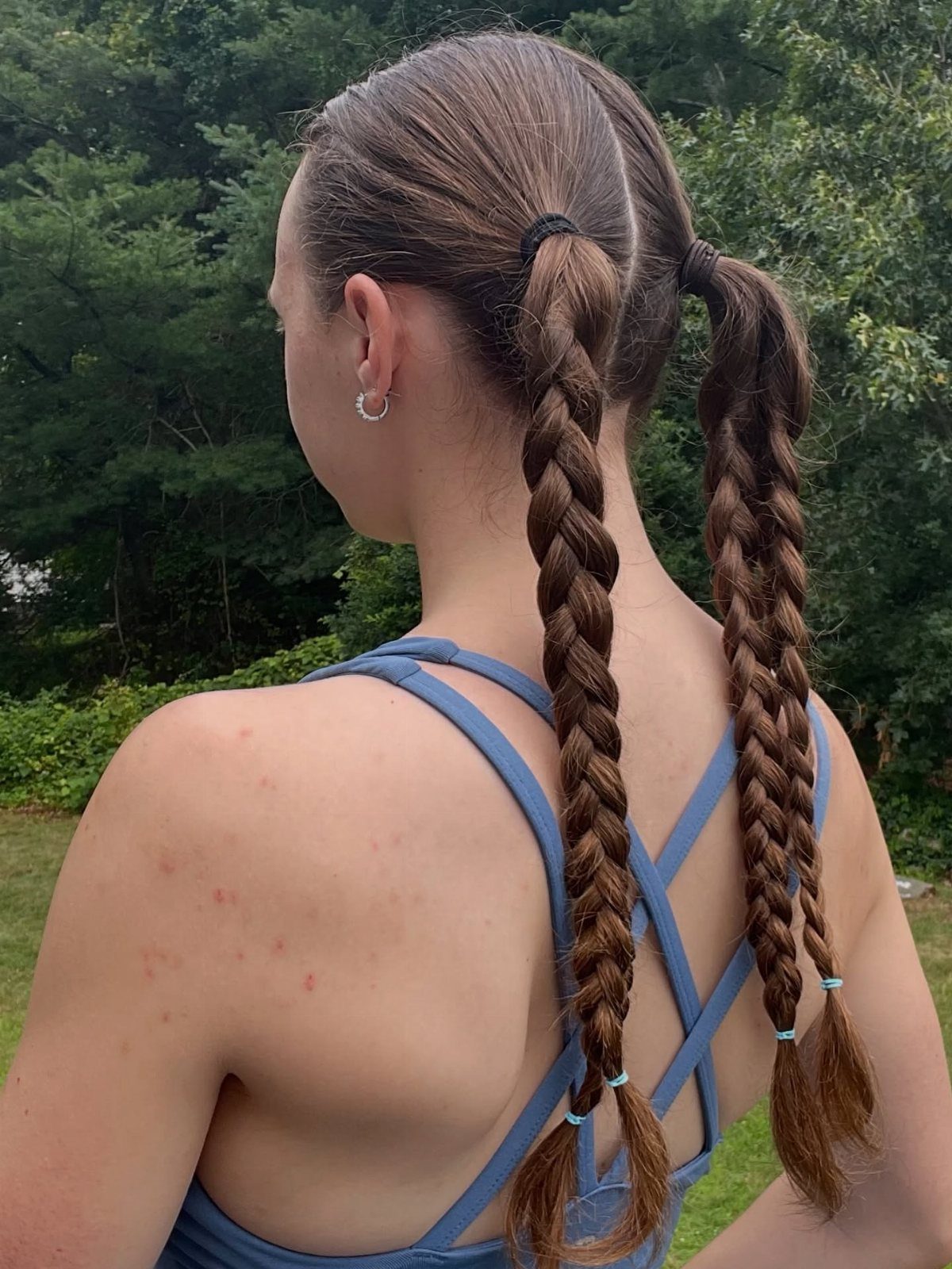 7 Clean Look Hair Ideas for Sleek Buns and Ponytails 6 Two tight braids on a woman with brown hair, viewed from behind outdoors.