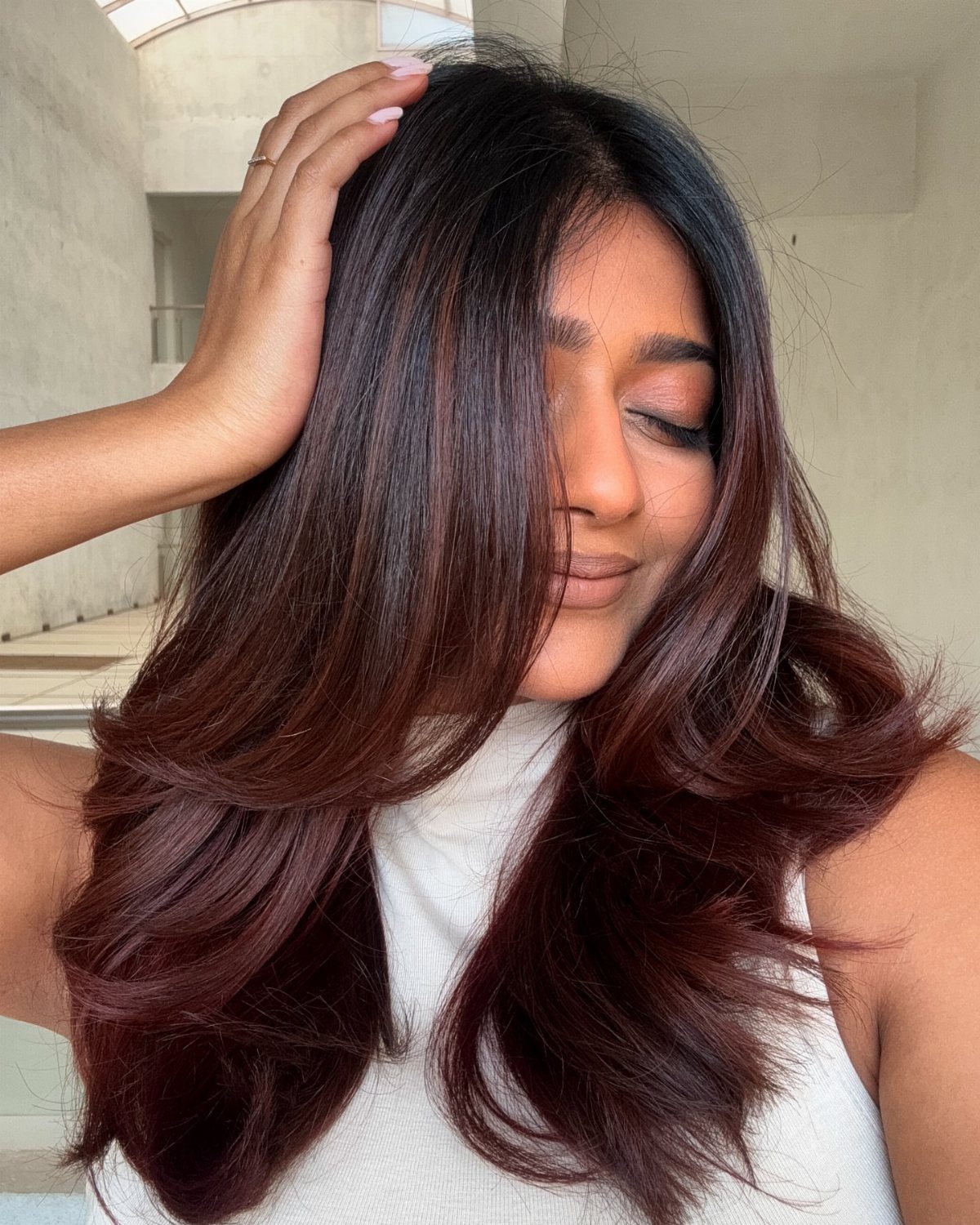 Color Hair for Morena: 8 Shades That Flatter Brown Skin 3 Woman with long wavy auburn hair posing in a white sleeveless top.