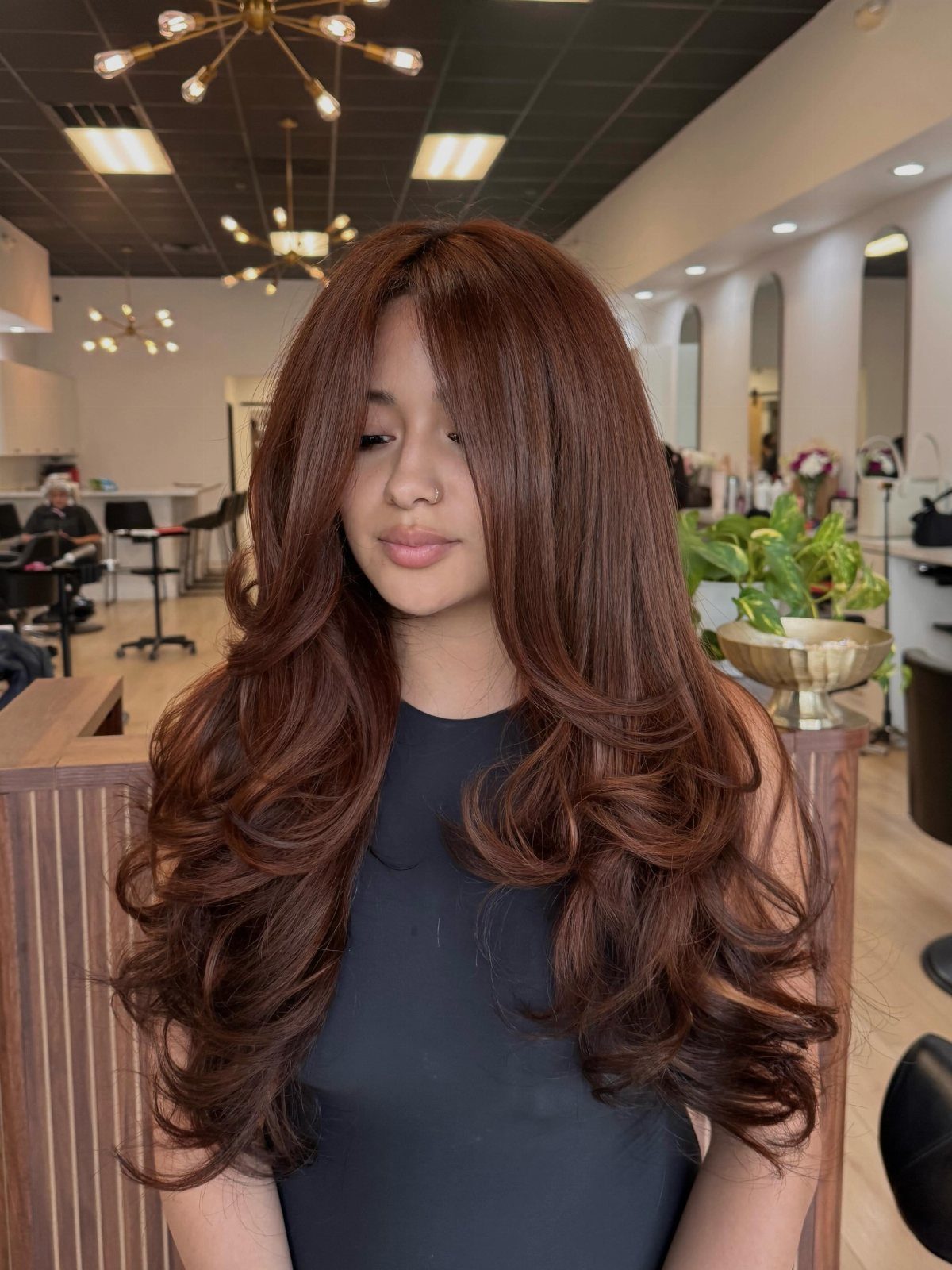 Color Hair for Morena: 8 Shades That Flatter Brown Skin 2 Woman with long, wavy chocolate brown hair posing in a modern hair salon.