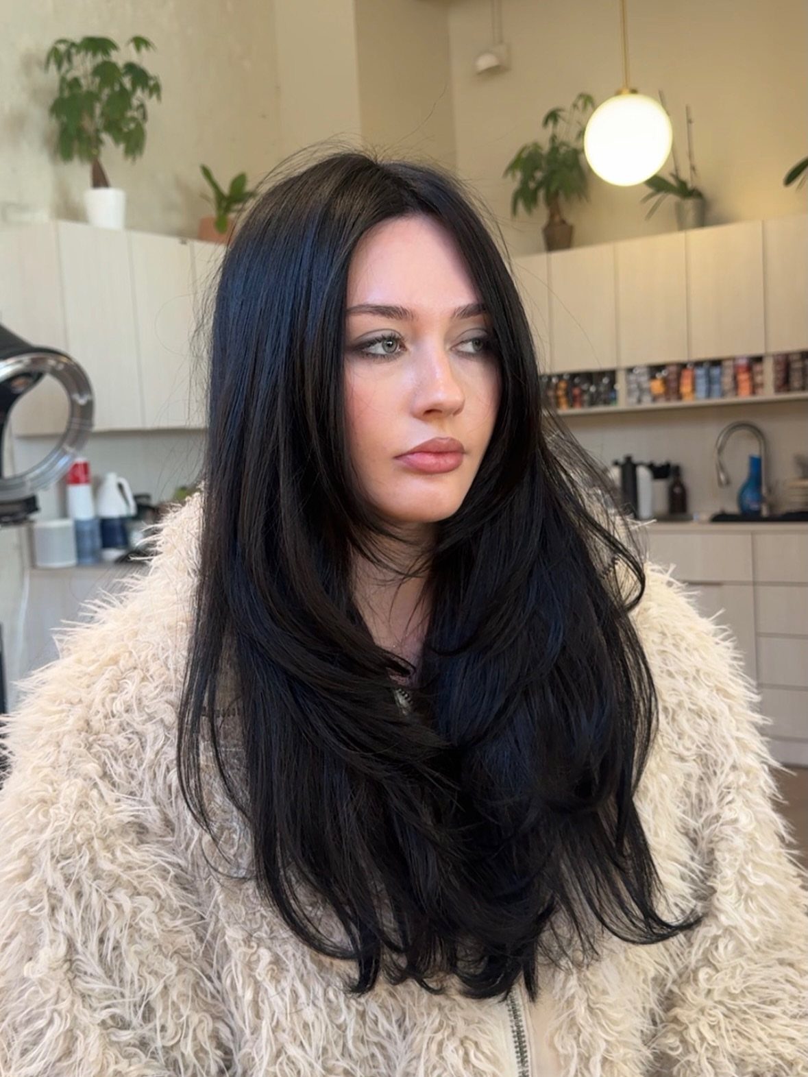 Color Hair for Morena: 8 Shades That Flatter Brown Skin 8 Woman with long soft black hair wearing a beige fuzzy coat indoors.