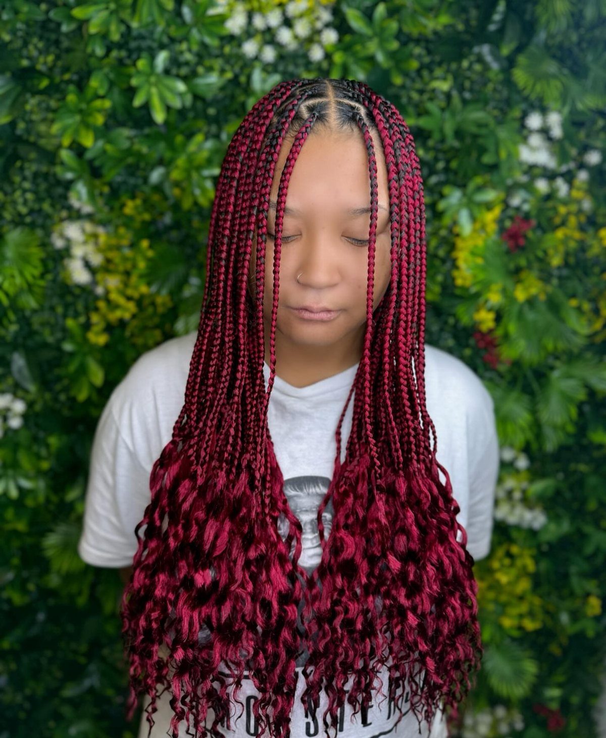 Cornrows Braids with Curls: 13 Ideas for Every Style 1 Person with burgundy cornrow braids transitioning into long, curly ends against green leaves.