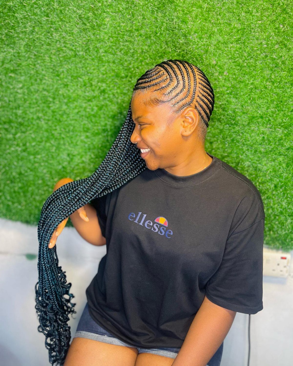 Cornrows Braids with Curls: 13 Ideas for Every Style 7 Woman with curved cornrow braids and curly ends posing against green grass wall