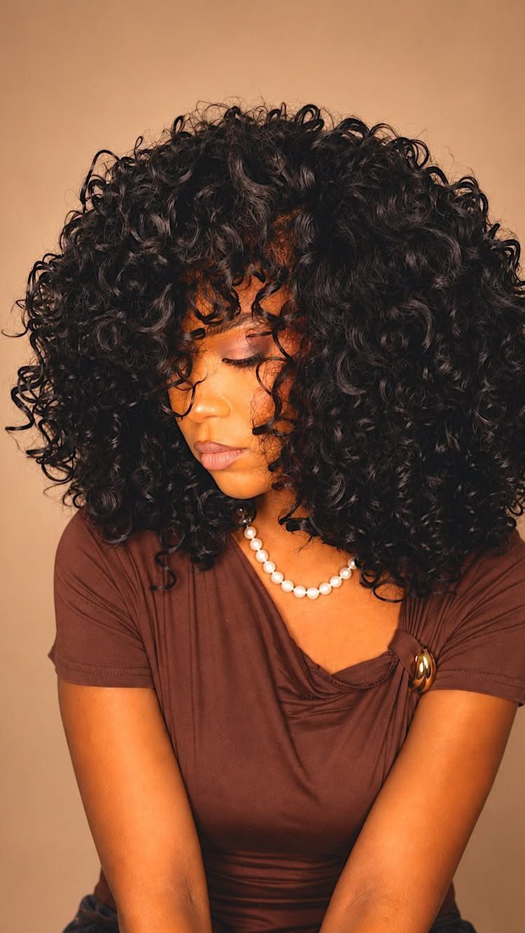 Curly Hair Beauty Ideas: 11 Styles, Colors and Care 11 Woman with voluminous black curly hair wearing a brown top and pearl necklace.