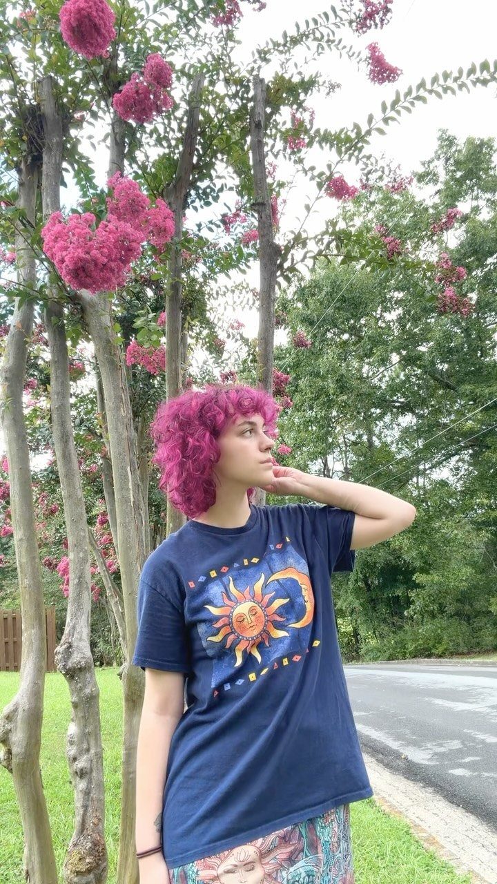 Curly Hair Beauty Ideas: 11 Styles, Colors and Care 6 Person with magenta curly hair posing outdoors next to pink flowering trees.