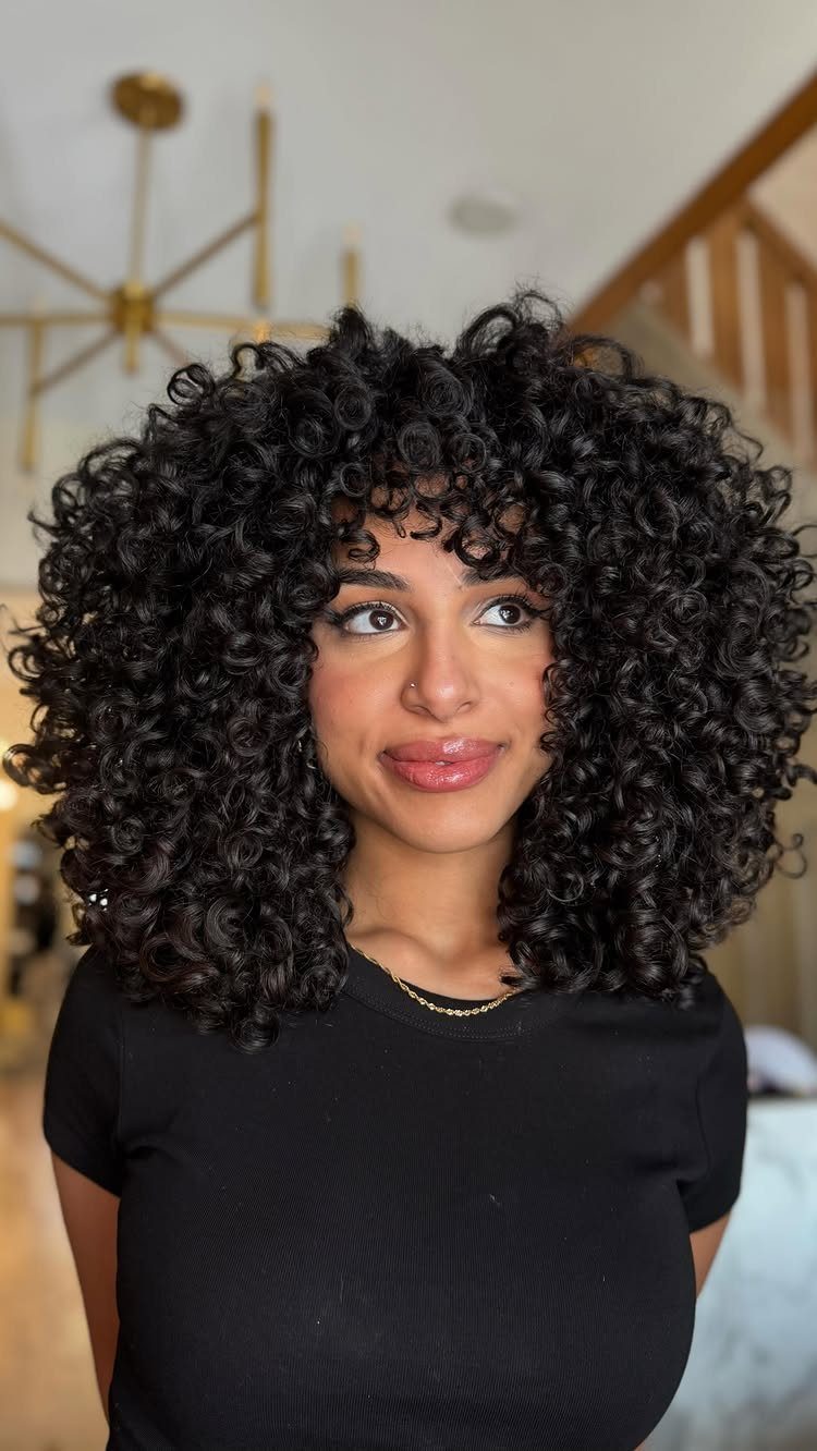 Curly Hair Beauty Ideas: 11 Styles, Colors and Care 4 Woman with voluminous dark curly hair and bangs wearing a black t-shirt.