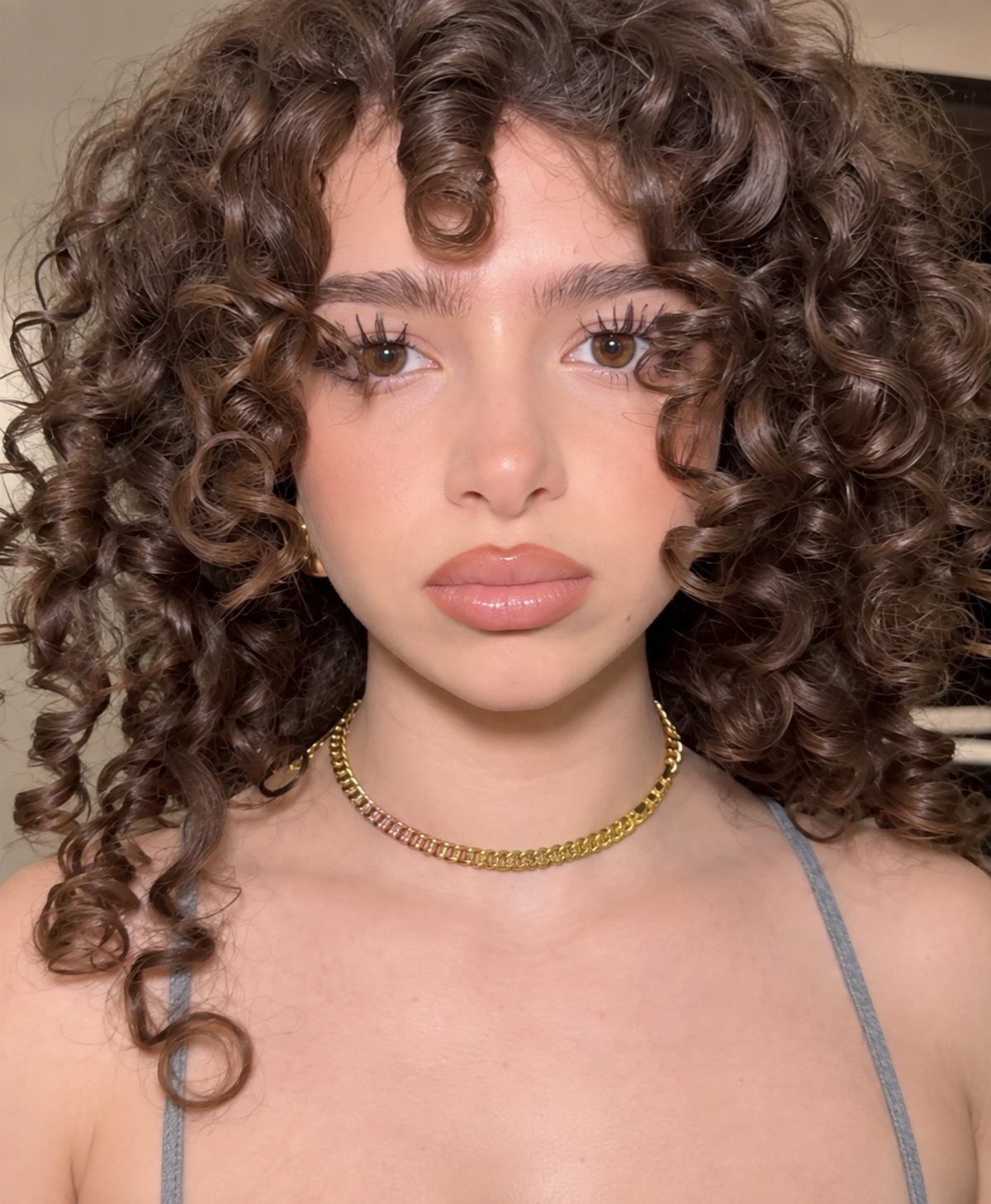Curly Hair Beauty Ideas: 11 Styles, Colors and Care 9 Young woman with voluminous brown curly hair wearing a gold chain necklace.