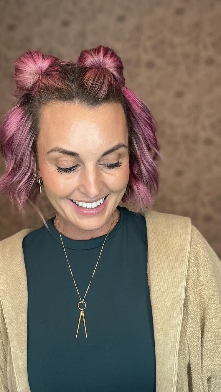 11 Cute Easy Work Hairstyles for Busy Mornings 10 Woman with pink hair styled in mini space buns smiling and looking down.