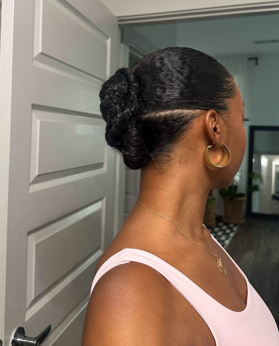 9 Cute Hair Styles for Church, From Buns to Box Braids 3 Woman with dark hair styled in a sleek, twisted low bun wearing gold jewelry.