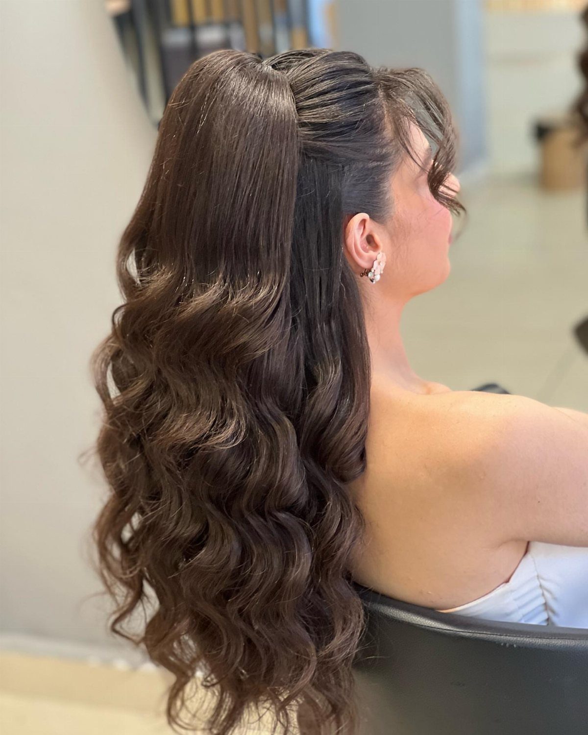 16 Cute Hairstyles for a Birthday Party, Waves to Braids 7 Woman with long brown wavy hair in an elegant half-up, half-down hairstyle.