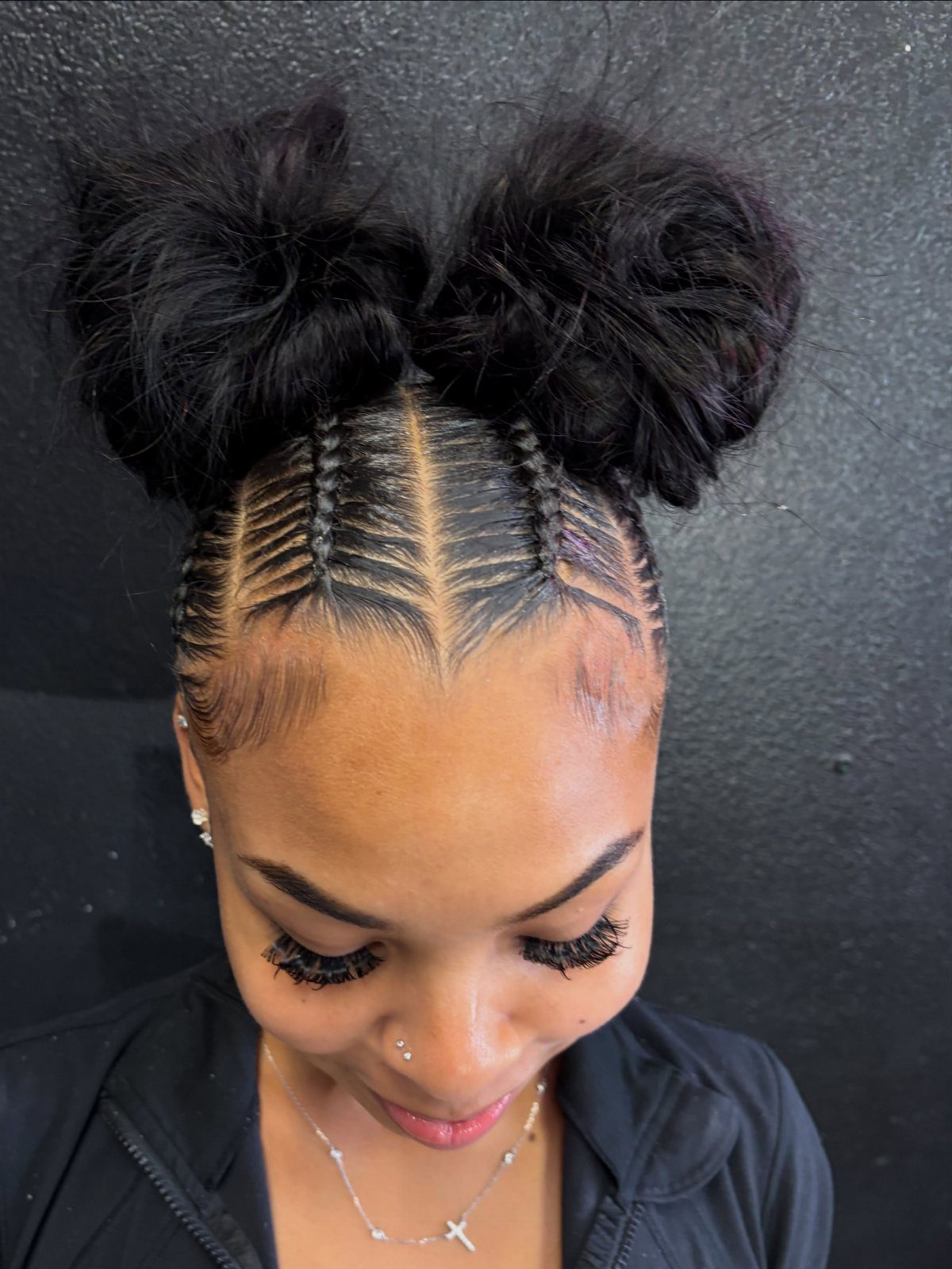 16 Cute Hairstyles for a Birthday Party, Waves to Braids 12 Woman with black hair styled in cornrows and two large fluffy space buns.
