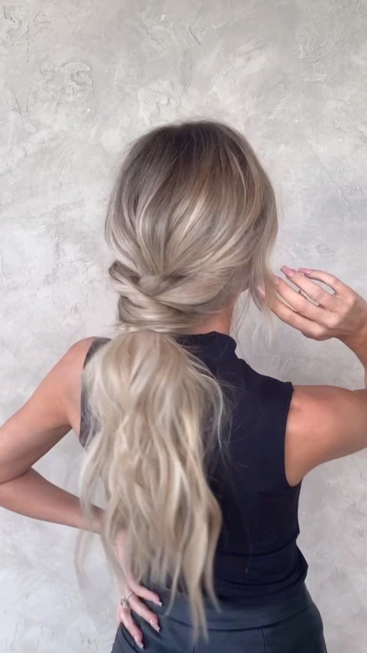 16 Cute Hairstyles for a Birthday Party, Waves to Braids 3 Blonde hair styled in a low twisted ponytail against a grey textured wall.