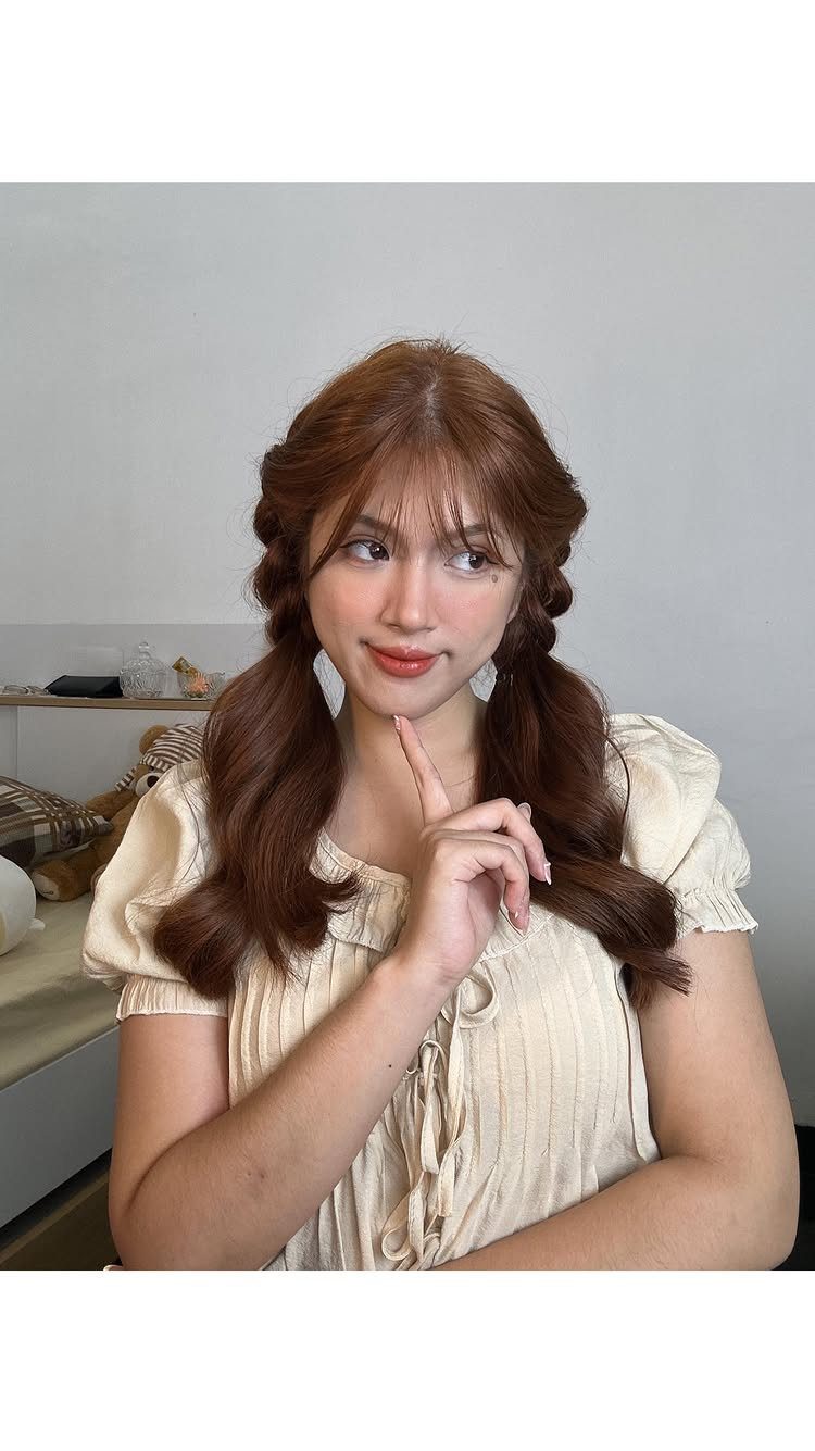 17 Cute Hairstyles for Picture Day, From Braids to Buns 12 Young woman with reddish-brown hair in braided pigtails wearing a cream ruffled blouse.