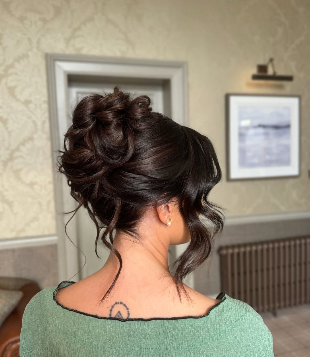 17 Cute Hairstyles for Picture Day, From Braids to Buns 6 Woman with dark brown hair styled in a voluminous high bun and loose curls.