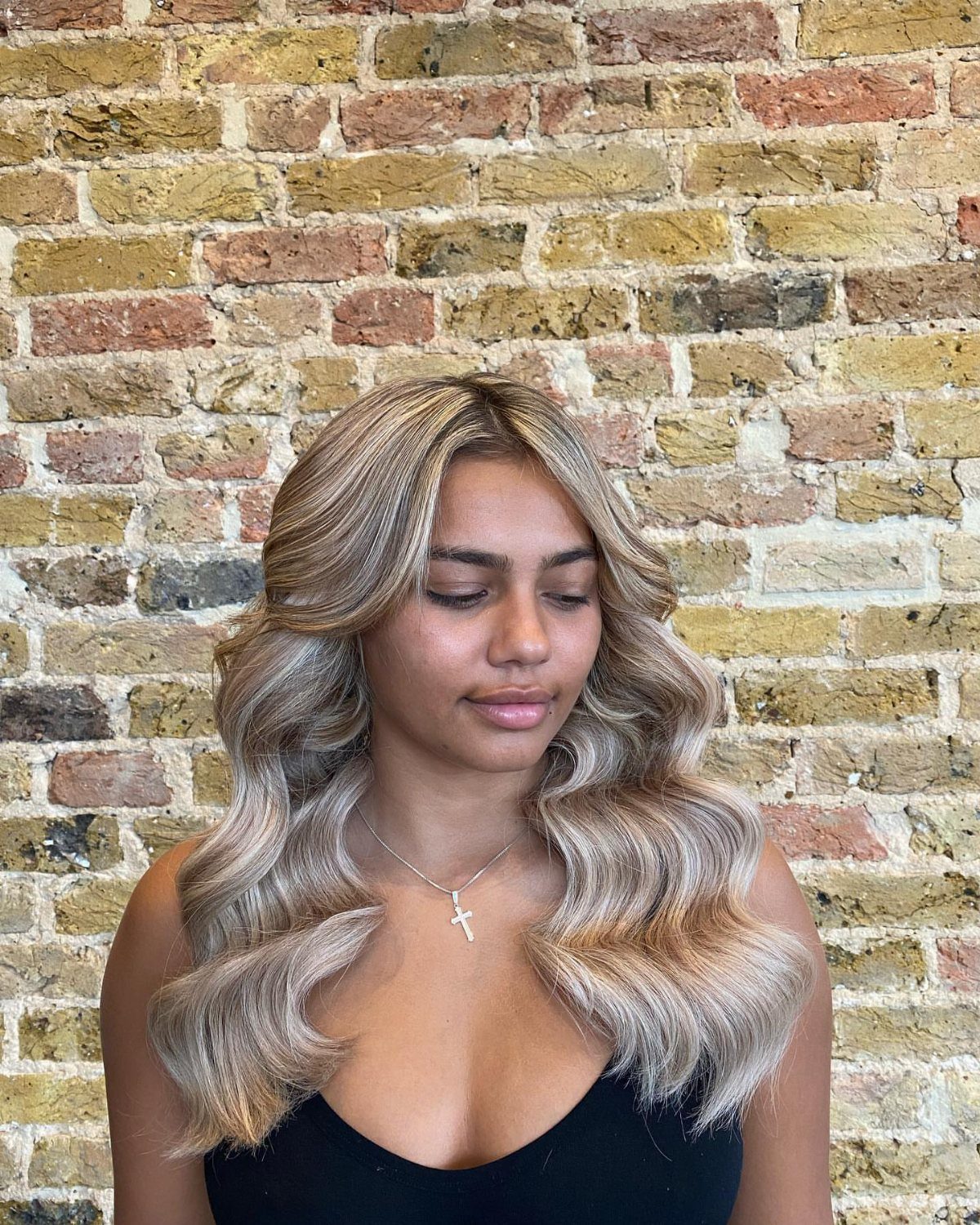 17 Cute Hairstyles for Picture Day, From Braids to Buns 7 Woman with long blonde highlighted hair styled in loose waves against brick wall