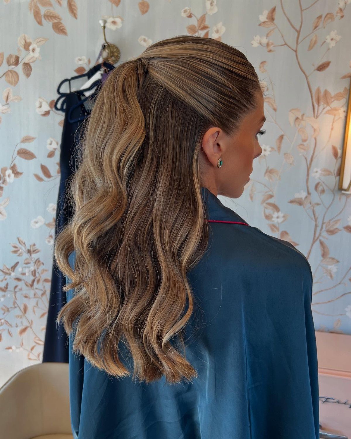 11 Cute Slick Backs: Braids, Buns, Ponytails and a Fade 3 Woman with blonde wavy hair styled in a half-up, half-down hairstyle wearing blue robe.