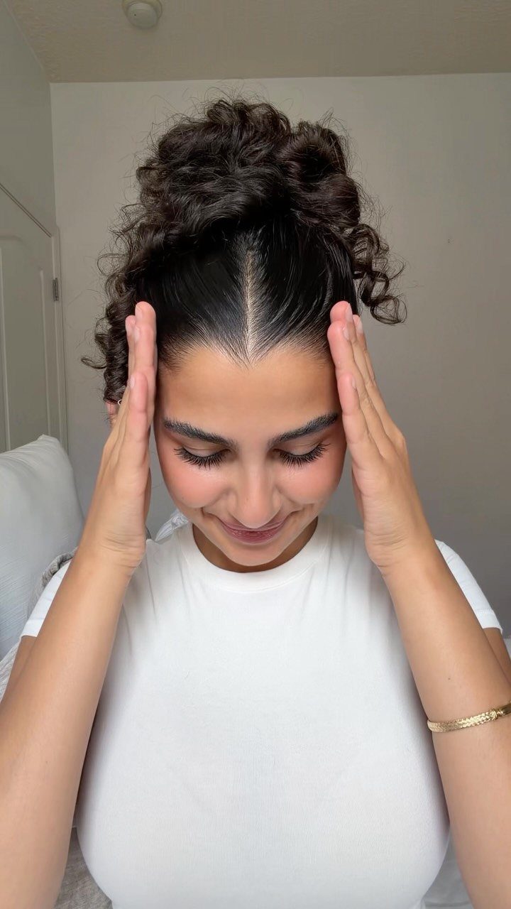 11 Cute Slick Backs: Braids, Buns, Ponytails and a Fade 7 Woman with slicked-back hair and a curly high bun wearing a white shirt