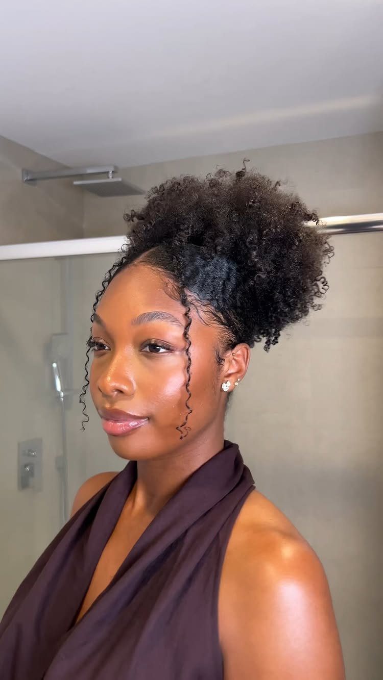 11 Cute Slick Backs: Braids, Buns, Ponytails and a Fade 4 Woman with slicked-back hair in a high curly puff and face-framing tendrils.