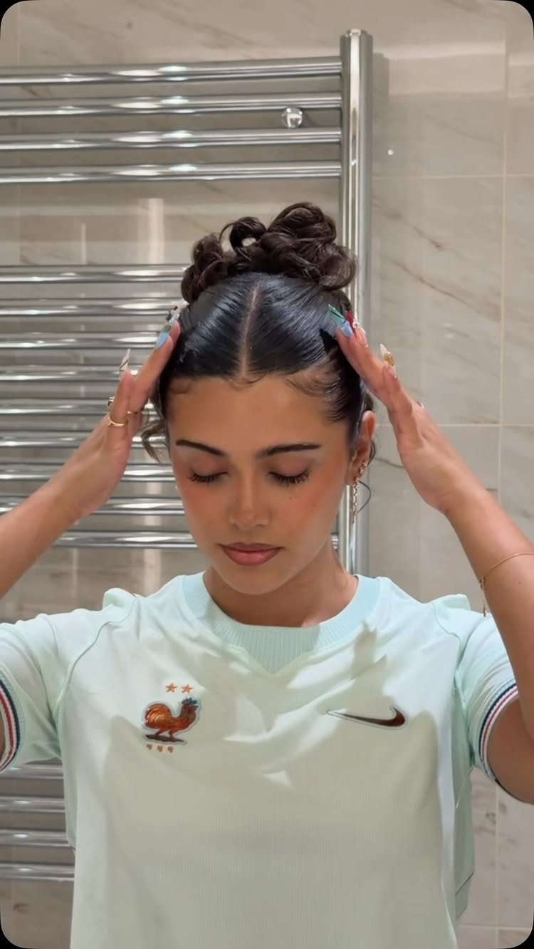 11 Cute Slick Backs: Braids, Buns, Ponytails and a Fade 10 Woman with a slicked-back high bun wearing a mint green t-shirt in a bathroom