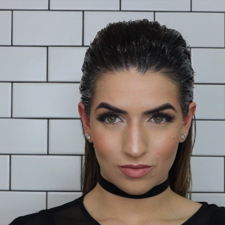 11 Cute Slick Backs: Braids, Buns, Ponytails and a Fade 5 Woman with wet-look slicked-back dark hair posing against a white tile wall.