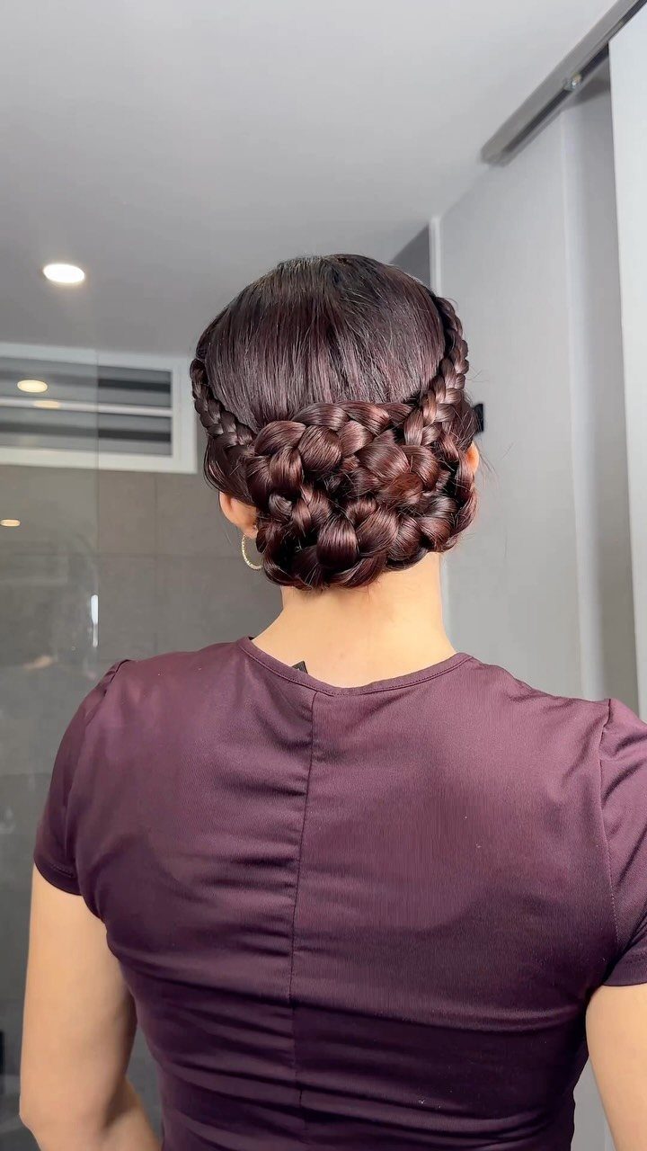 Intricate braided bun hairstyle on dark brown hair with a maroon top.