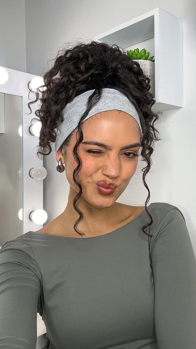 Woman with curly hair in a high messy bun and grey headband.