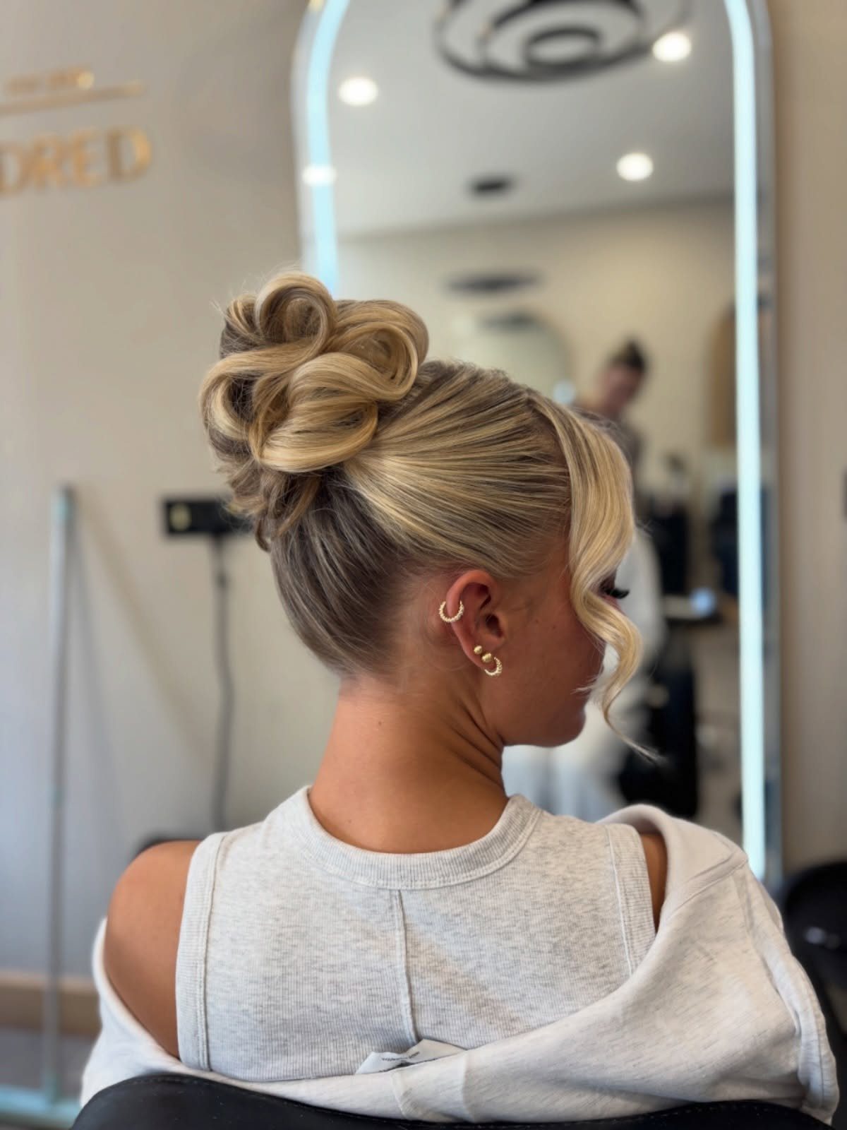 Blonde woman with a high looped bun and a face-framing curl.