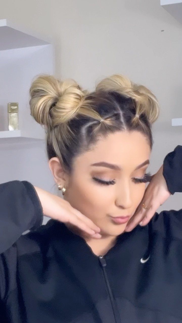 12 Cute Updo Hairstyles for Easy Everyday Styling 8 Woman with blonde hair styled in two space buns wearing a black jacket.